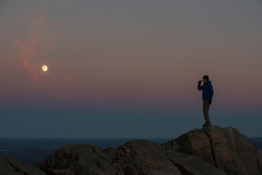 A Hiker Enjoying A Nip Of Whiskey And Watching The Moonrise At Sunset