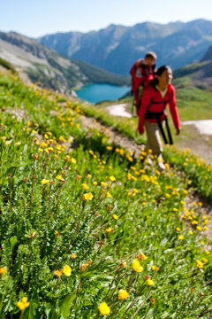 A mother carries her child in her backpack through a meadow over Trail Rider Pass by Snowmass Lake during a multiday backpacking trip in the Maroon Bells in Snowmass Wilderness jus