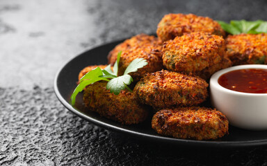 Carrot and spinach vegan vegetarian bites with sweet chili sauce in a black plate