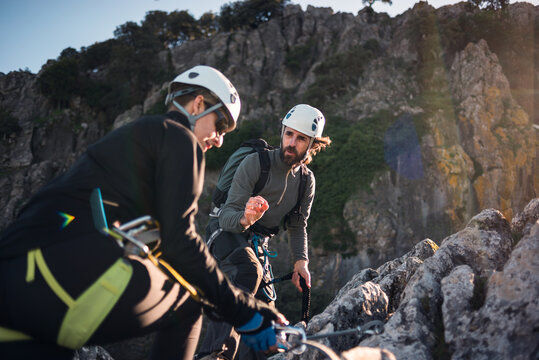 Concept: adventure. Man and woman with helmet, harness. Explaining climbing techniques. Solar luminous flare.Via ferrata in the mountains.