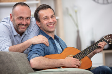 Fototapeta premium young gay couple sitting on sofa and playing guitar