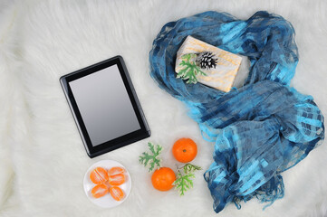Digital tablet mockup with blank screen, fresh mandarins ,gift and blue- turquoise silk print scarf for lady on white fur background. Top view. Free copy space. Lifestyle concept.