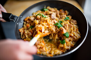 Woman cooking tasty Stew with meat and cabbage in pan on kitchen