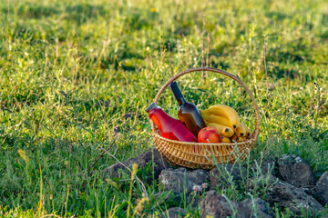 picnic basket with wine, juice and fruits on green grass