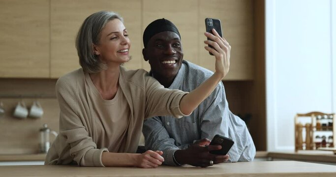 Happy multiethnic couple have fun use smartphone spend leisure together at home, Caucasian wife makes selfie picture staring at cellphone screen enjoy time on internet with African husband. Tech usage