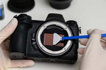 Hands hold a professional sensor cleaning swab and clean the matrix from dust and dirt.Cleaning and maintenance of the mirrorless camera sensor. Care concept for professional photography equipment. 