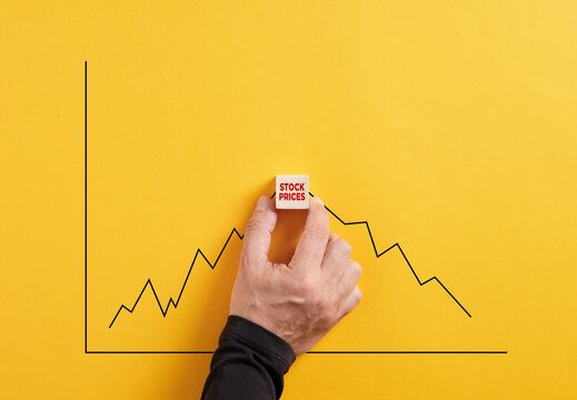 Predicting the crisis in stock market prices. Crisis and stock exchange decline forecast. Hand holds the wooden cube with the word stock prices with an increasing and declining graph.