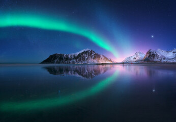 Fototapeta na wymiar Aurora borealis and beach in Lofoten islands, Norway. Beautiful northern lights. Starry sky with polar lights. Night winter landscape with aurora, sea with sky reflection, city lights, snowy mountains