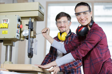 female worker using bench drill with colleague