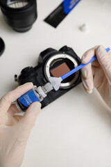 Hands holding sensor cleaning swab and applying a special cleaner to clean the camera sensor. Cleaning and maintaining the mirrorless camera sensor.Care for professional photographic equipment.