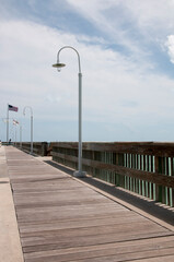 A wooden pier with flag street lamps in the background against the cloudy sky