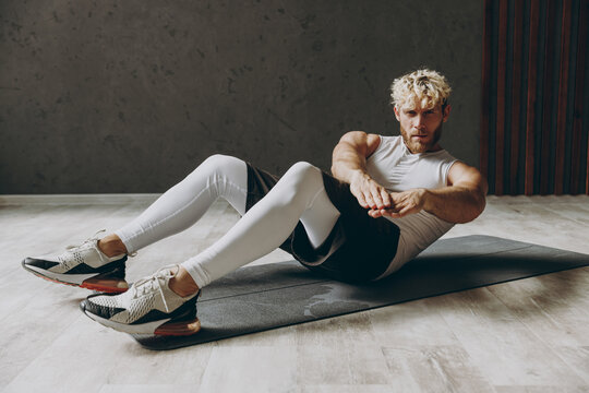 Full body sideways young strong sporty athletic sportsman man wear white tank shirt black shorts do abdominal abs exercises at floor, pump side press warm up train indoor at gym Workout sport concept.