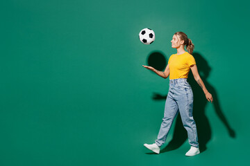 Fototapeta na wymiar Full body profile happy young woman fan wear yellow t-shirt cheer up support football sport team hold in hand soccer ball watch tv live stream walk go throw up ball isolated on dark green background.