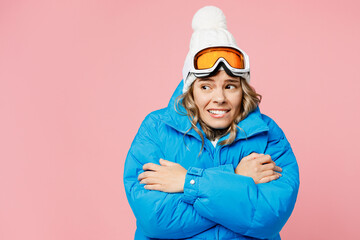 Snowboarder sad woman wears blue suit goggles mask hat ski padded jacket hold herself warming look aside isolated on plain pastel pink background Winter extreme sport hobby weekend trip relax concept