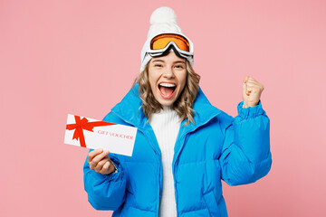 Snowboarder woman wear blue suit goggles mask hat ski padded jacket hold store gift coupon voucher card isolated on plain pastel pink background. Winter extreme sport hobby weekend trip relax concept.