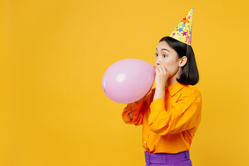 Side view happy fun young woman of Asian ethnicity wears casual clothes cap hat celebrating blowing...