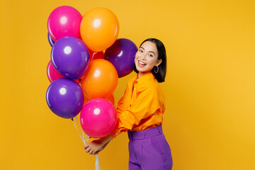 Fototapeta na wymiar Side view happy fun smiling young woman wearing casual clothes celebrating holding bunch of colorful air balloons look camera isolated on plain yellow background. Birthday 8 14 holiday party concept.
