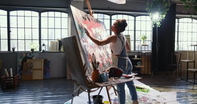Female artist working on abstract impressionist painting. Woman artist works with spatula drawing abstract picture and expressing her mental state. Talented artist paints emotional picture. Modern art