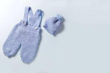 Blue knitted baby romper and newborn cap, flatlay.