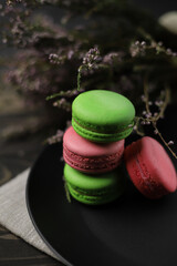 traditional American macaroons in pink and bright green color on a wooden background and a black plate next to purple fragrant flowers