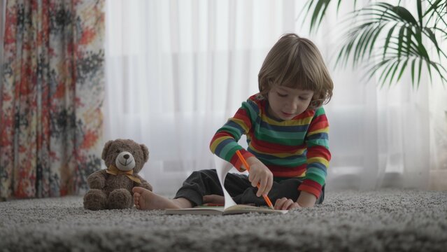Portrait of little child sit on carpet and draw a note book