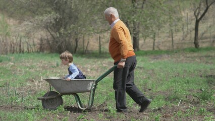Old man carrying little kid in wheelbarrow