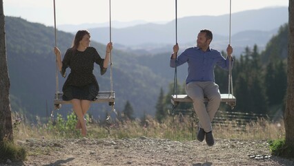 Happy lovers couple in rope wooden swings in a spectacular mountain scenery