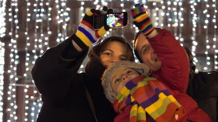 Happy family taking a selfie, Christmas tree lights in background, smiling