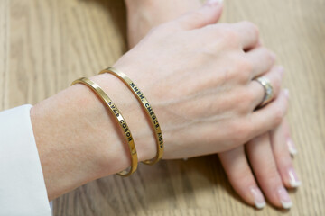 Womans hands with two thin gold bracelets. The inscription on the bracelet in Russian Live, laugh, love, be yourself. Simple jewelry with printed inscription.