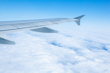 Obraz premium Wing of an airplane flying over white clouds and blue sky
