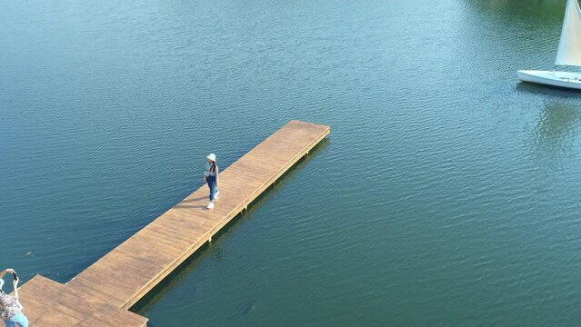 Asian girl is walking on a wooden bridge that extends over the lake and taking pictures with her mother.