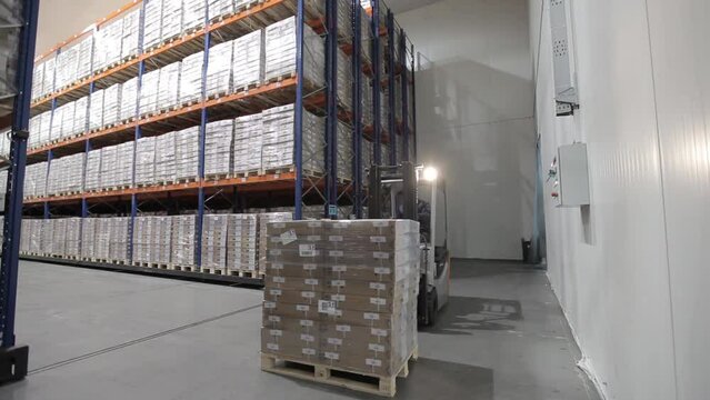 Forklift loads a pallet of boxes and merchandise in a logistics warehouse. Cardboard boxes on racks of merchandise