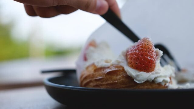 A person's hand is using a spoon to scoop strawberries on top of the choux cream and enjoy it.