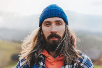 Portrait of attractive man with long hair wearing blue hat and jacket with mountain on the background. Man hiker staing with beautifule view on the mountains. © fifeflyingfife
