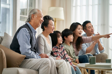 three generation asian family watching tv together at home - obrazy, fototapety, plakaty