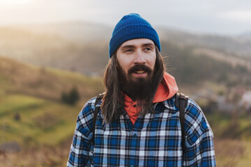 Portrait of hiker - man hiking on mountains. Handsome male traveler photographer looking to the side walking on hills wearing blue beanie