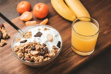 Granola cereal oatmeal with white yogurt, chocolate, banana fruit and nuts in a bowl on dark wooden board