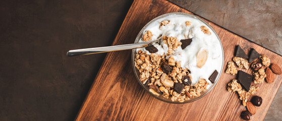 Granola cereal oatmeal with white yogurt, chocolate, fruist and nuts in a bowl on dark wooden board, top view - Powered by Adobe
