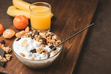 Granola cereal oatmeal with white yogurt, chocolate, banana fruit and nuts in a bowl on dark wooden...