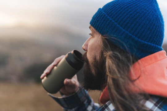 Portrait of photographer male drinking water while making a stop during a walk the backdrop of beautiful mountain landscape and looks into the distance.