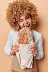 Curly woman bites delicious freshly baked gluten free sourdough loaf of bread eats healthy homemade...