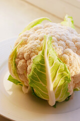 Cauliflower on a white platter with a green leaf close-up. Beautiful veins of green leaf on the head of cauliflower