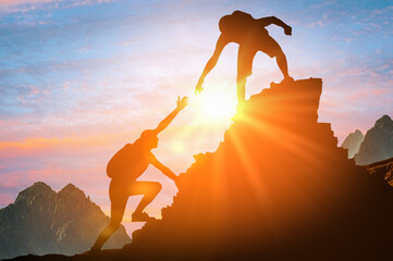 Man is giving helping hand. Silhouettes of people climbing on mountain at sunset. Help and...