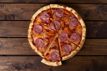 Pizza on a plate on a wooden background, cut into pieces