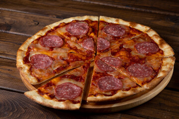 Pizza on a plate on a wooden background, cut into pieces