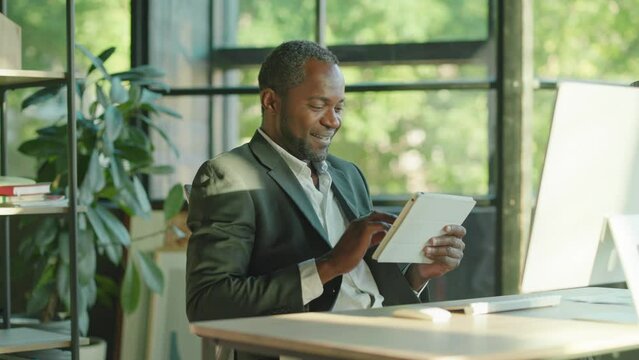 Happy african american man with a beard working using a tablet computer smiling at the sunlight in office technology businessman. Worker. Portrait. Slow motion