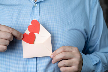 The concept of the Valentine's Day holiday. Men's hands hold an envelope with a paper heart. The...