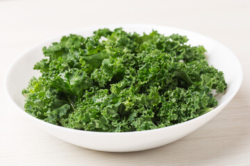 Salad with curly kale, olive oil in a white bowl on a light wooden background. Healthy eating concept. Superfoods. Organic food.
