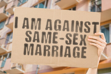 The phrase " I am against same-sex marriage " is on a banner in men's hands with blurred background. Wed. Loving. Emotional. Emotion. Heart. Engaged. Spouse. Partner. Union. Finding. Discover. Unity