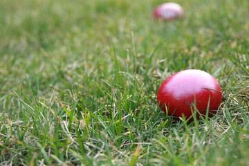 Wielkanoc. Czerwone jajko wielkanocne leży na trawie na pierwszym planie. Z tyłu drugie kolorowe jajko